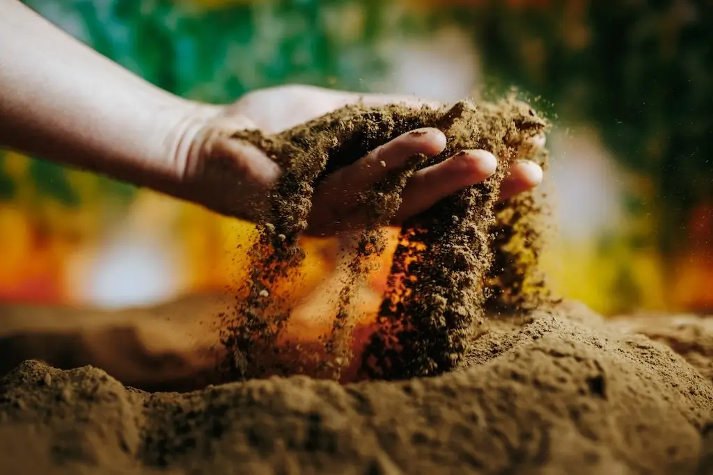 A hand gently sifting through soil, demonstrating the importance of healthy soil in eco friendly lawn care.