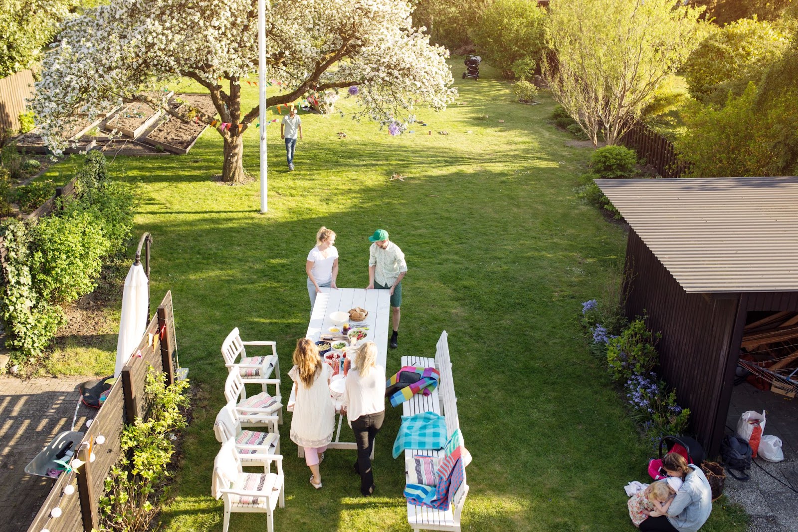 Family and friends enjoying an outdoor gathering under a blooming tree in a well-maintained backyard, showcasing the results of a thorough summer lawn treatment.